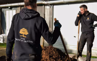 Deux équipiers en sweat au logo de l’entreprise, pelle en main, devant un tas de paillage