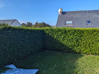 Haies d’angle hirsutes autour d’une pelouse, maison en ardoise derrière