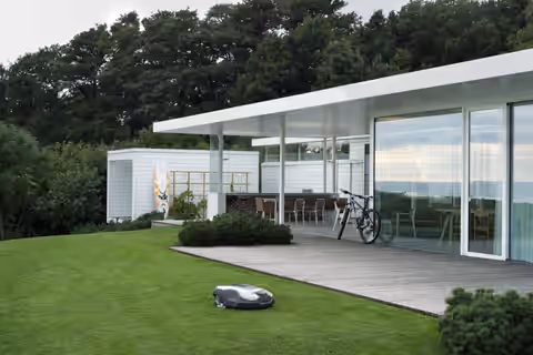 Robot tondeuse Husqvarna Automower sur une pelouse devant une maison contemporaine (visuel Husqvarna)